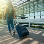 A woman walks with a suitcase outside an airport terminal, ready for travel.