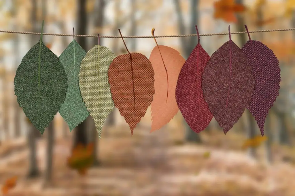 Fabric leaves hang on a rope, showcasing autumn colors in a forest backdrop.