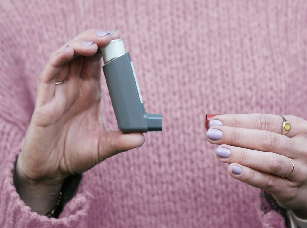 Woman holding a gray inhaler against a pink sweater. Essential asthma medication concept.