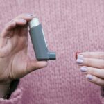 Woman holding a gray inhaler against a pink sweater. Essential asthma medication concept.