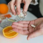 Close-up of a person taking a vitamin capsule with citrus fruit and medication on a table.