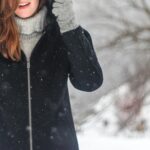 A woman enjoying a snowy winter day, dressed warmly and smiling.