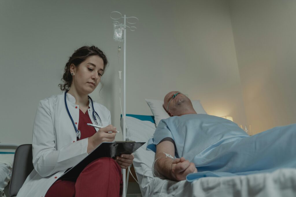 A female doctor checks a medical chart beside a male patient in a hospital room.