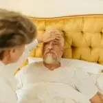 Elderly man in bed receiving care from a woman at home.