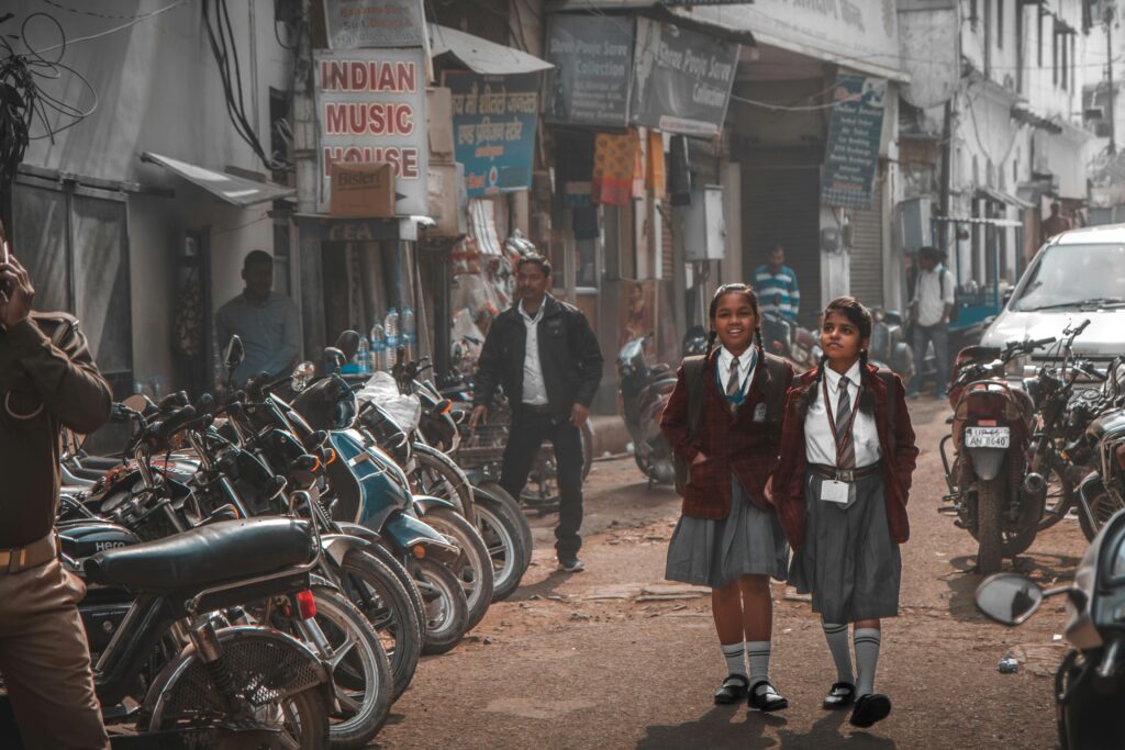 Two schoolgirls in uniform walking along a busy street in Amritsar, India.