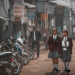 Two schoolgirls in uniform walking along a busy street in Amritsar, India.