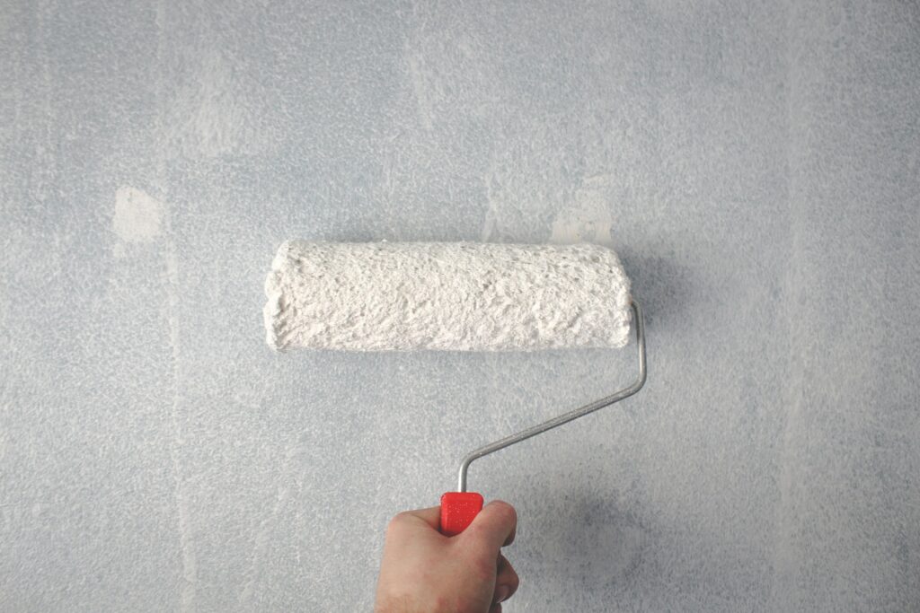 A person's hand using a paint roller to apply white paint on a wall.