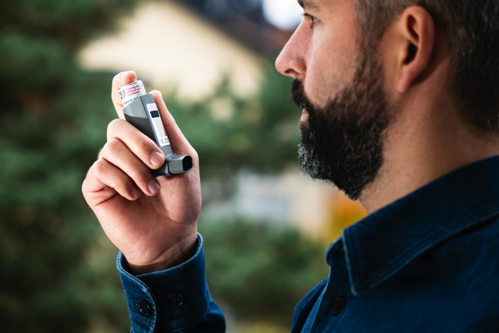 Adult man uses inhaler outdoors for asthma relief, focusing on respiratory health.