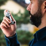 Adult man uses inhaler outdoors for asthma relief, focusing on respiratory health.