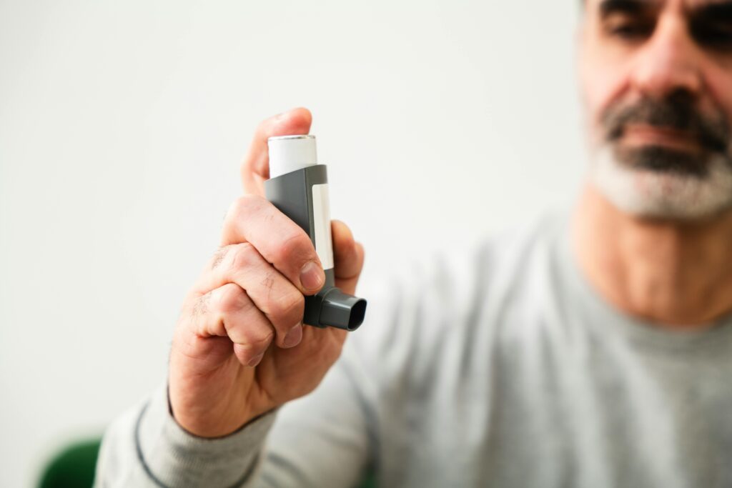 Middle-aged man using an inhaler to manage respiratory issues indoors.