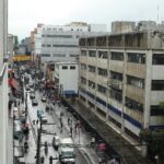 Street view of a bustling city under rain, showcasing diverse pedestrians and urban life.