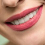 Vivid close-up image of a woman's smile showcasing red lipstick and white teeth on a light background.