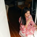 A young woman in a checkered shirt sitting indoors, enjoying a refreshing drink.