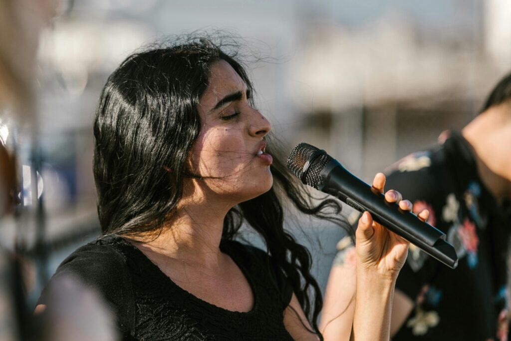 A young woman passionately sings into a microphone during an outdoor performance.