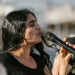 A young woman passionately sings into a microphone during an outdoor performance.