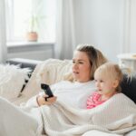 A mother and daughter cuddled on the couch under a blanket, enjoying TV time.