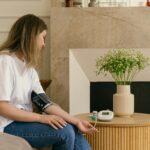 Caucasian woman checking blood pressure with a sphygmomanometer by a vase of flowers indoors.