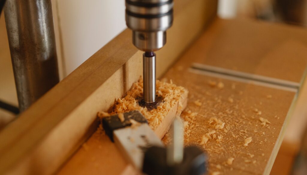 Steel boring machine with milling cutter drilling hole in wooden plank in modern joinery studio