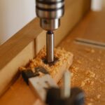 Steel boring machine with milling cutter drilling hole in wooden plank in modern joinery studio