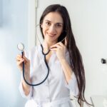 Confident female doctor holding a stethoscope while smiling in a clinic setting.